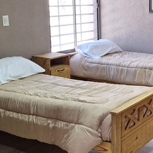 Habitación triple luminosa con cama, armario, mesa de luz, aire acondicionado y ventana grande en la residencia para mayores Casa Trapiche.