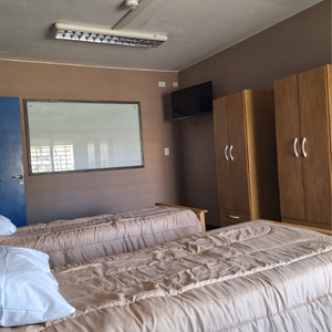 Habitación triple luminosa con cama, armario, mesa de luz, aire acondicionado y ventana grande en la residencia para mayores Casa Trapiche.